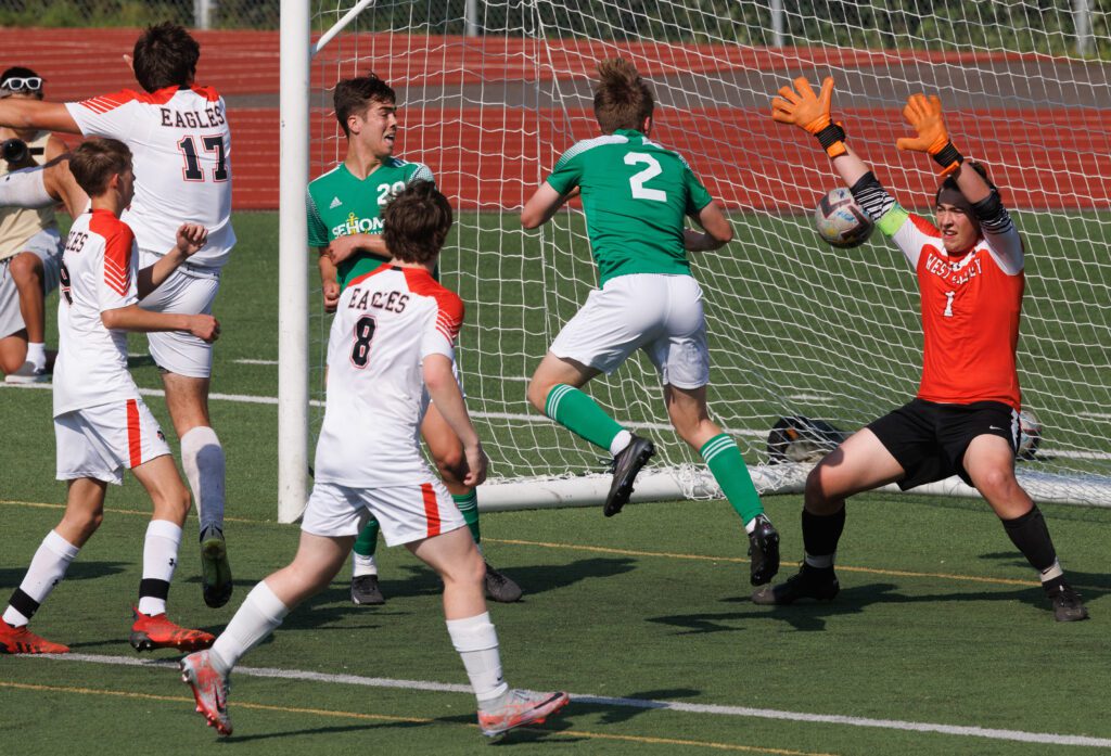 Sehome's Noah Allen heads the ball in hopes of scoring as other players surround the goal net while the goalie raises his hands to try and block the shot.