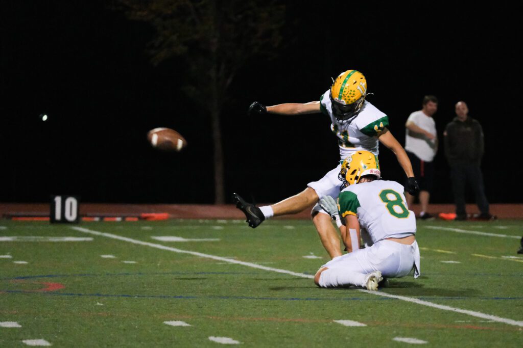 Lynden senior kicker Troy Petz kicks the ball at Civic Stadium as another player kneels next to him to hold the ball.