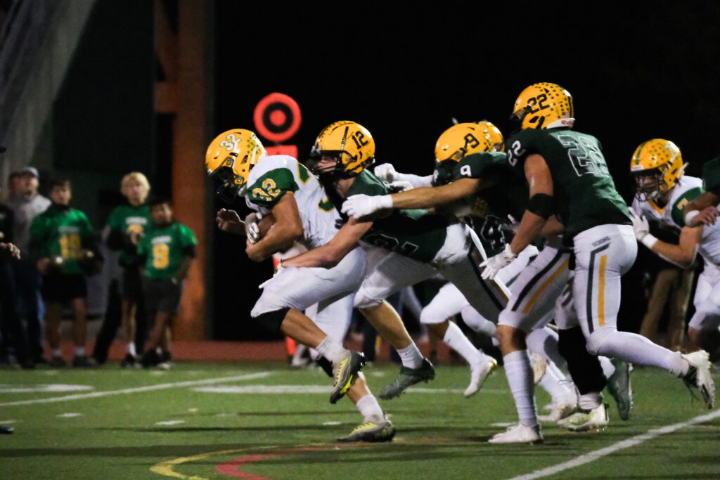 Lynden senior running away from the opposing team as a player tackles him from the back while spectators watch.