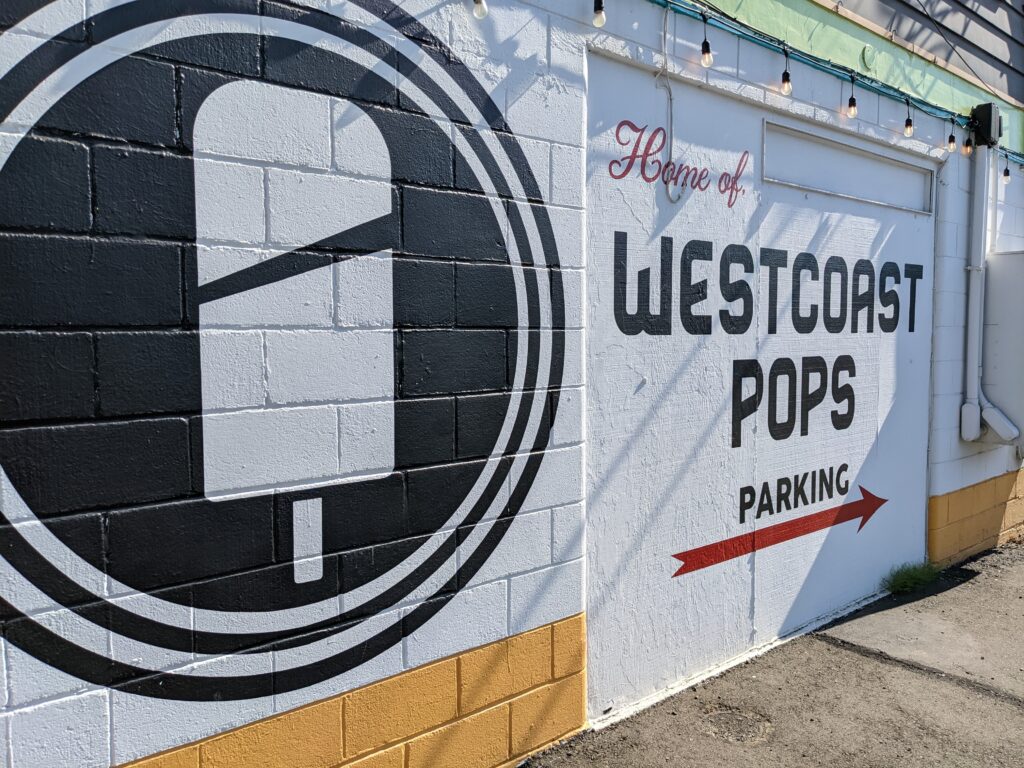 The outdoor wall of westcoast pops shows visitors where to park next to their business logo.