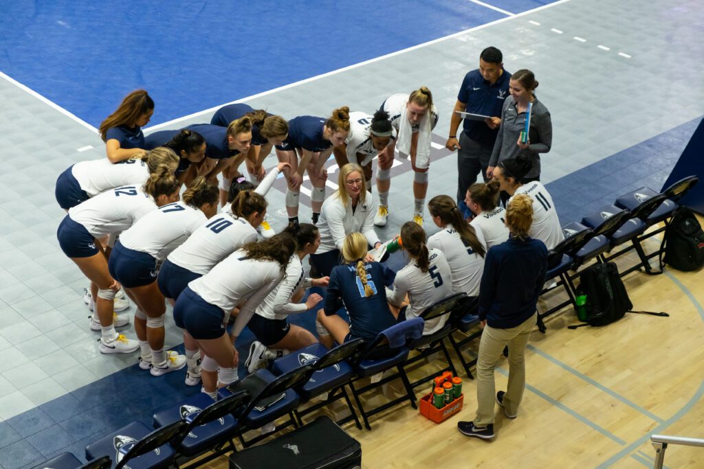 A coach goes over a plan surrounded by her all female volleyball team.