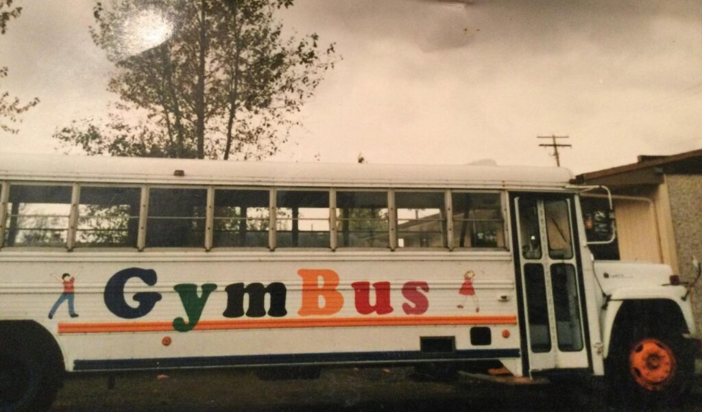 A white bus with colorful letters on the side reading Gym Bus.