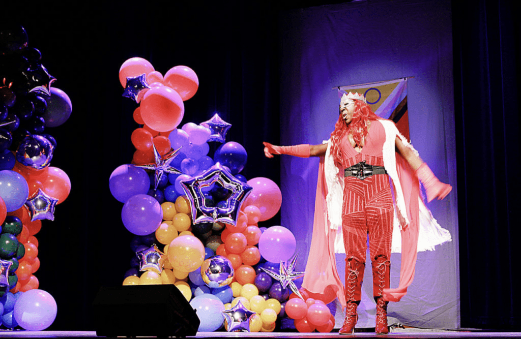 Quintessa Touché points to the audience next to an assortment of balloons of different shapes and colors.