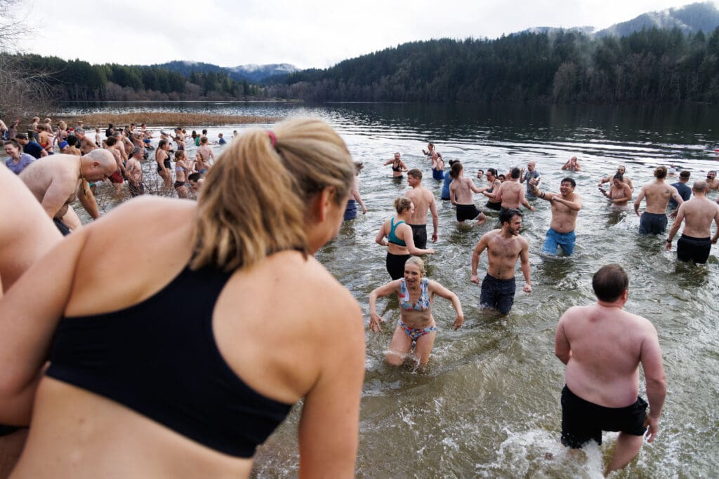 Hundreds of people enter and exit the chilly water of Lake Padden, all dressed in swimming attire.