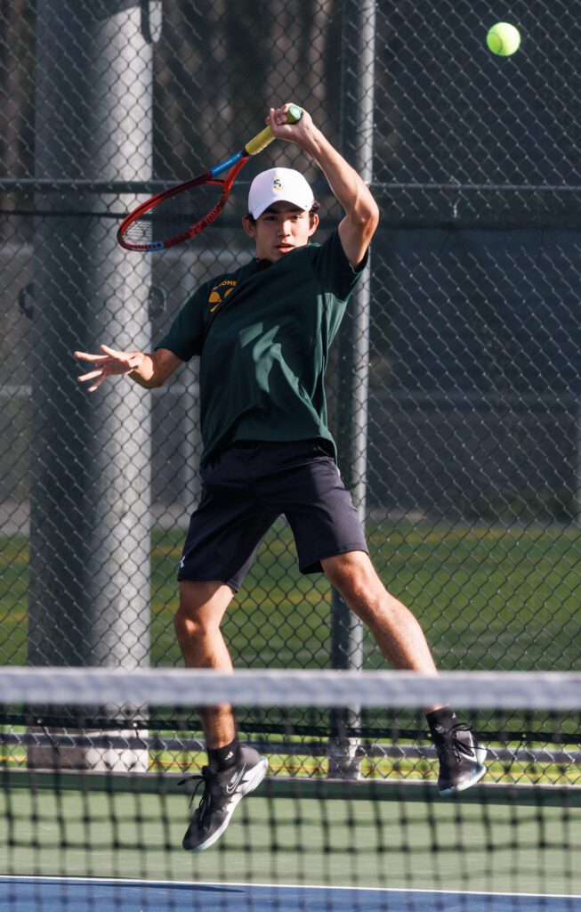 Sehome’s Zach Chai leaps backwards as he returns a volley with a red tennis racket.