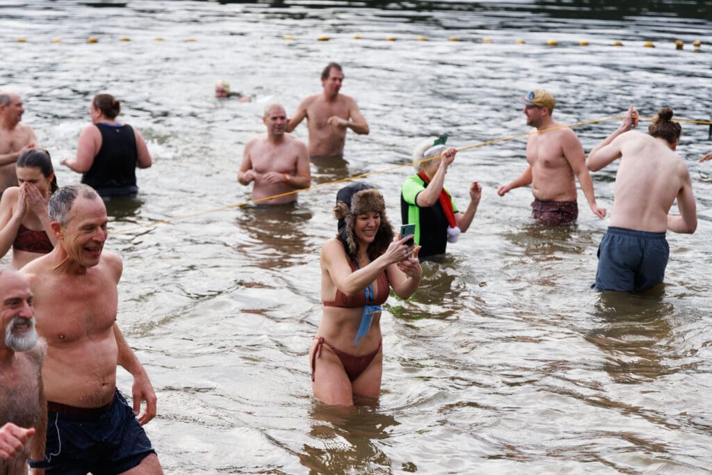 Teresa Wolf takes a selfie while sporting a winter hat in Lake Padden surrounded by other attendees.