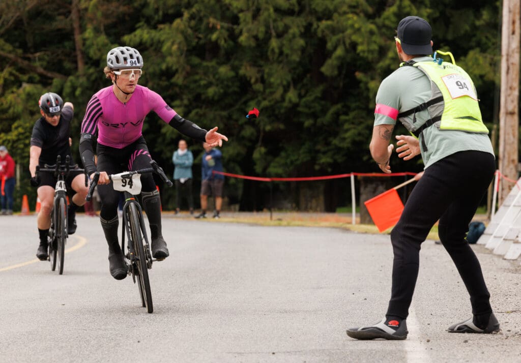 Biker Jack Bardi throws the timing chip to his Compass teammate during the bike-to-canoe exchange of the May 2022 Ski to Sea race in Everson.