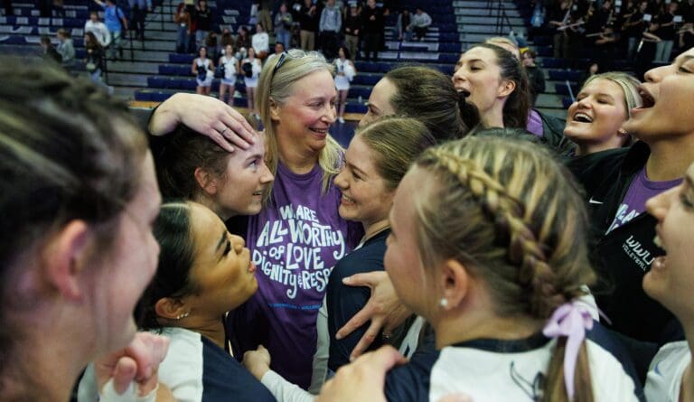 Western Washington University volleyball head coach Diane Flick-Williams celebrates with her team in a close huddle as she hugs her players.