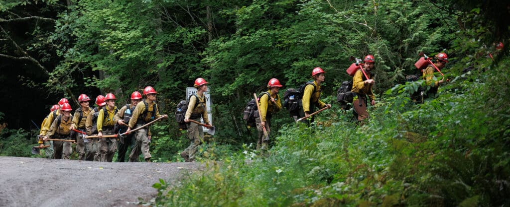 The Baker River Hotshots, all wearing red safety hard hats, head to their trucks to head hom in a single line.