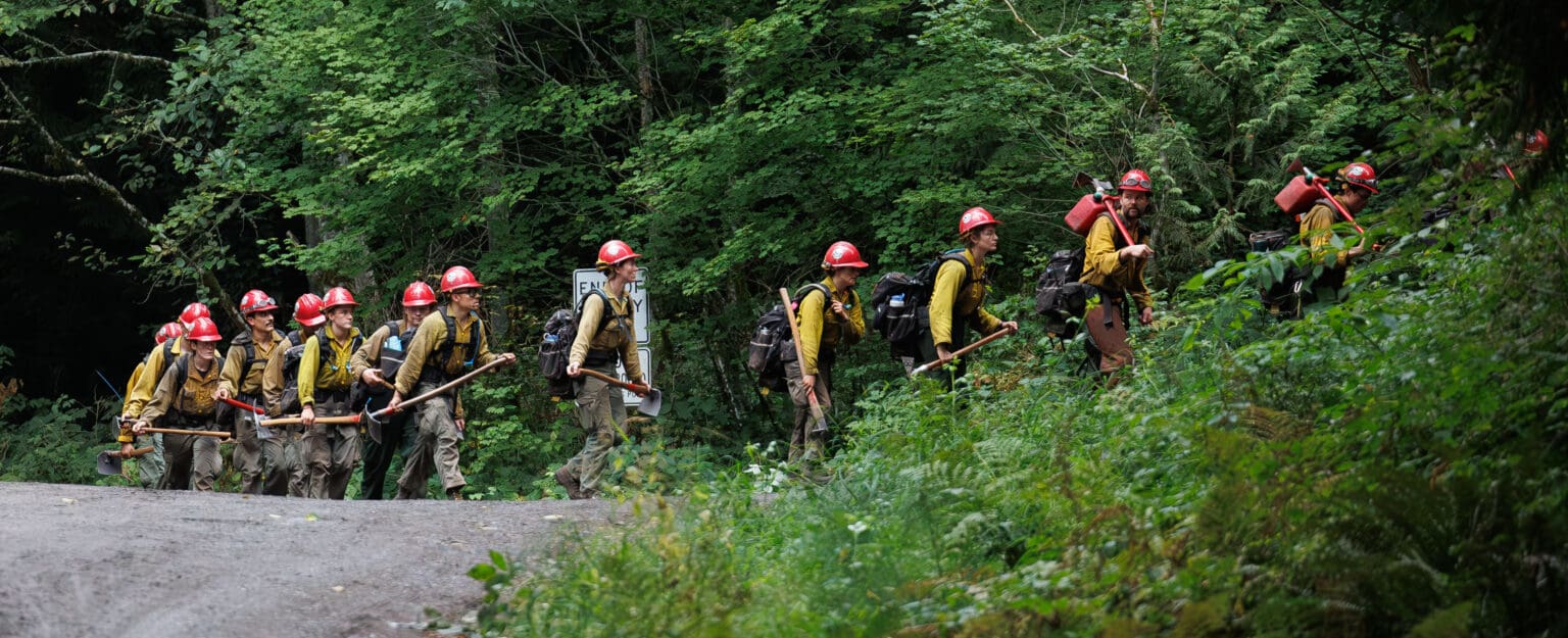 The Baker River Hotshots, all wearing red safety hard hats, head to their trucks to head hom in a single line.