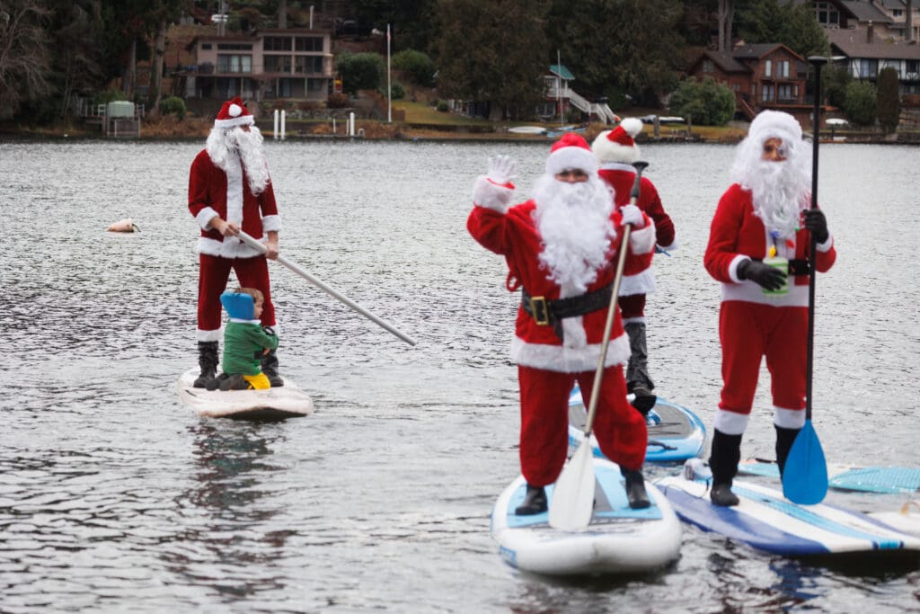 Micah Ping uses a PVC pipe as an oar as he tries to catch up to other santa claus paddlers who are waving at the camera.