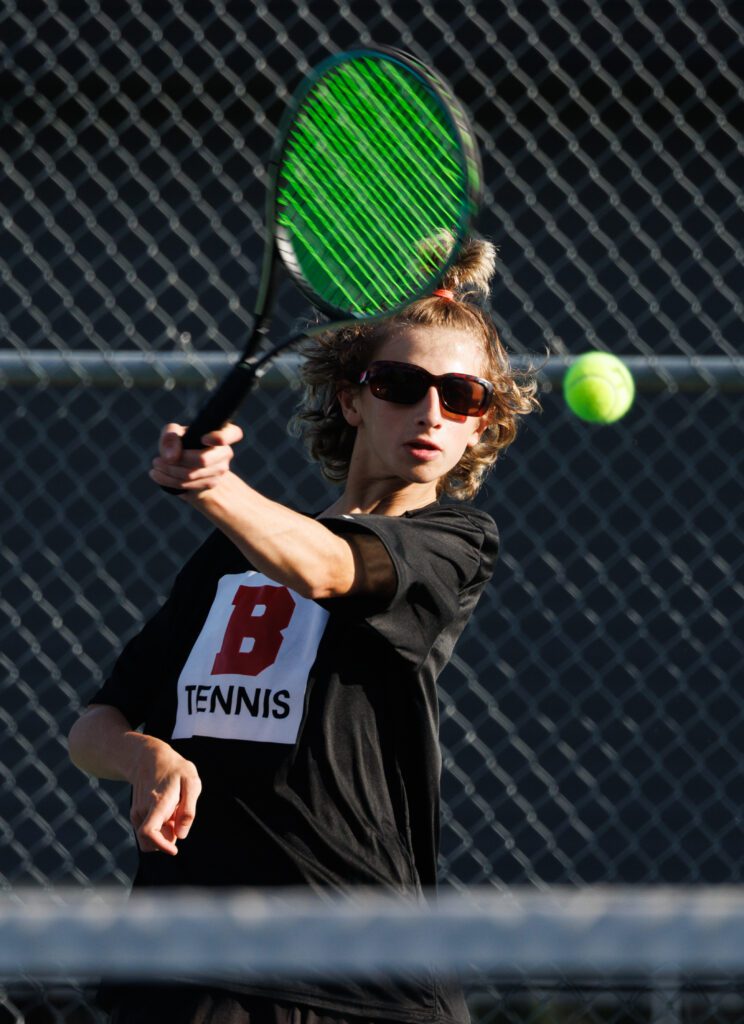 Bellingham’s Zach Lyne returns a shot with his tennis racket while wearing sunglasses to shield his eyes from the sun.
