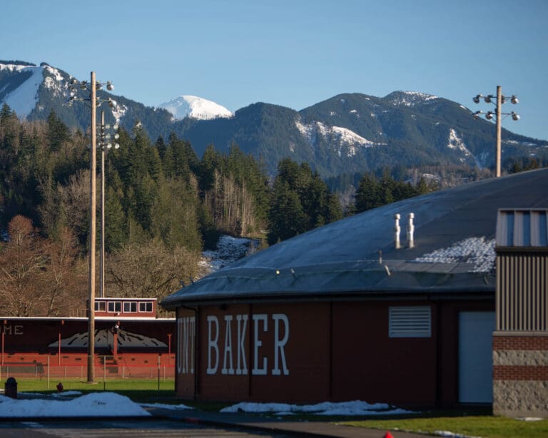 Mount Baker School building with its name painted on has the mountains and dense forests in the background.