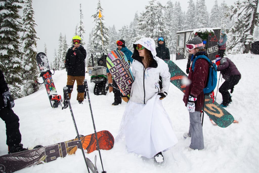 Tara Ortiz grabs her board to hit the slopes with her family in her wedding dress as she is surrounded by snowboarders and skiers.