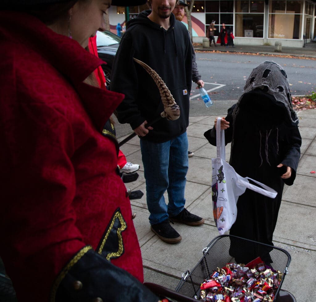 A child dressed as a grim reaper picks up candy from Erika Millage at Third Planet.