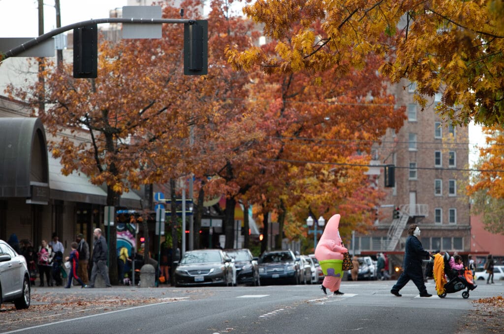 Patrick Star and Mike Myers psuh a stroller across Magnolia Street leaving behind a group of halloween participants.