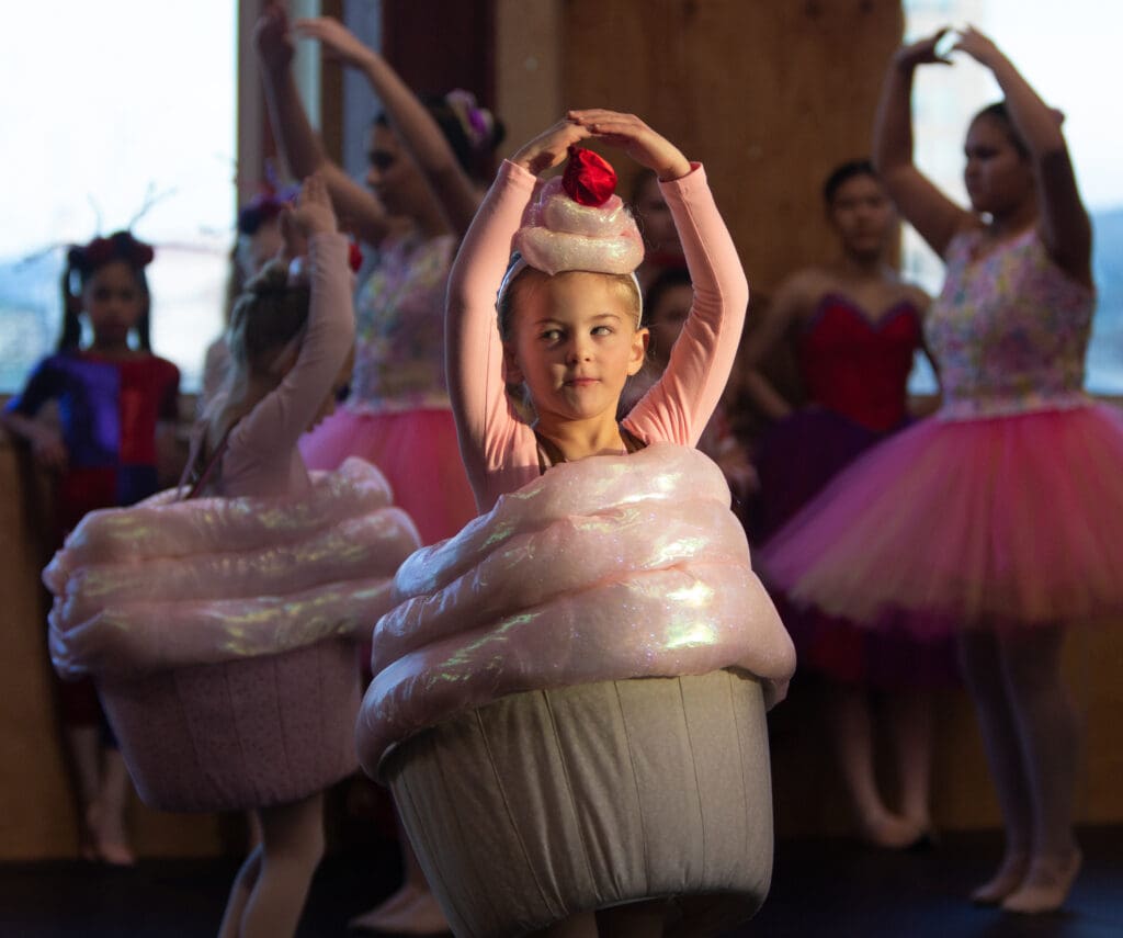 A young girl in a cupcake outfit spins during rehearsal of Opus Performing Arts' near her peers who are dressed in similar costumes.