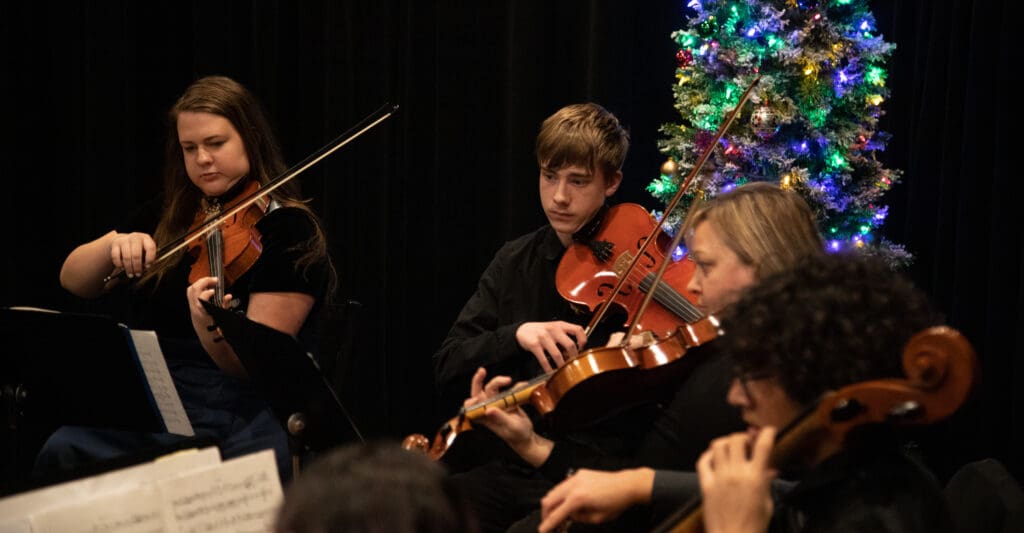 The Squalicum Chamber Orchestra performs with violins next to a christmas tree.