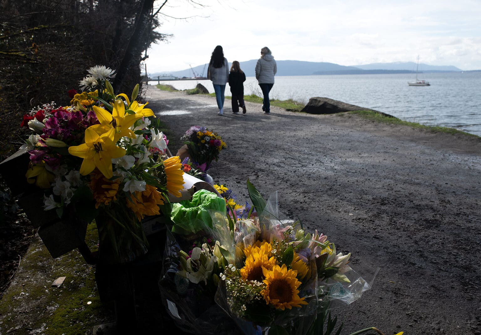 A family that stopped to look at the memorial walks past the bench that Henry King frequented near Taylor Dock where bouquets of flowers are placed to honor him.