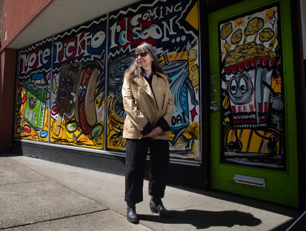 Susie Purves stands in front of 105 Grand Ave. where the windows and doors have cartoon confectionary painted colorfully.