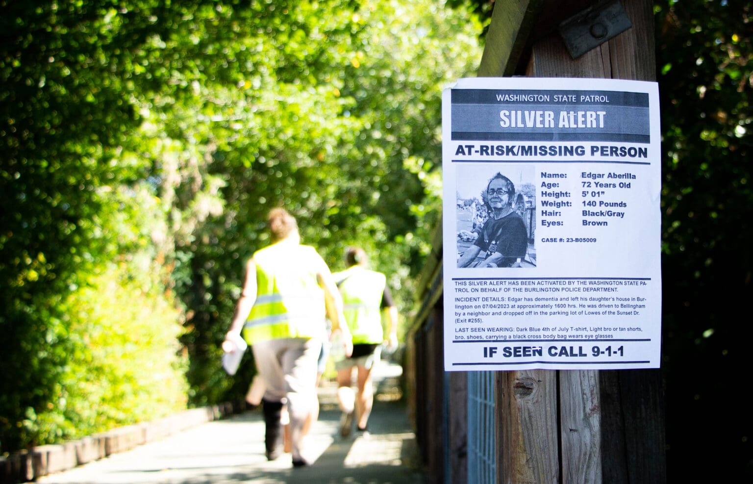 A missing person flyer is posted on a pole as people walk by in hopes of finding the missing elderly man.