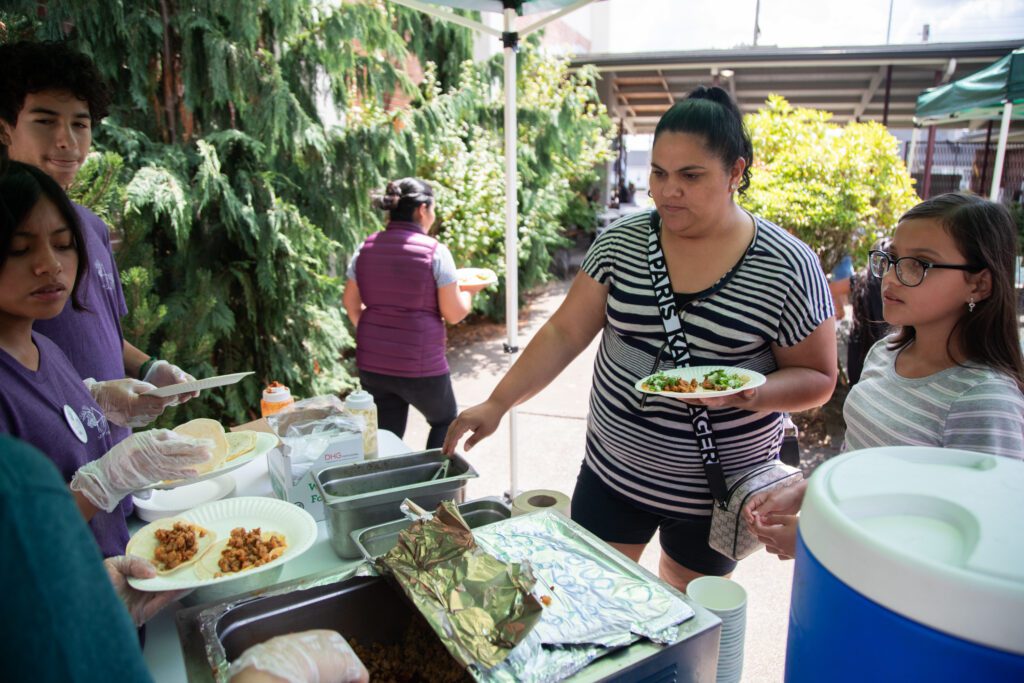 Diana Salcido, left, and Corina Ibarra get plates of tacos as volunteers continue to prepare plates of tacos for the next person.