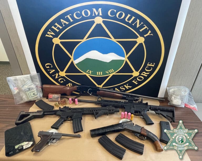 Firearms, suspected fentanyl and cash laid out on a table in front of Whatcom County logo.