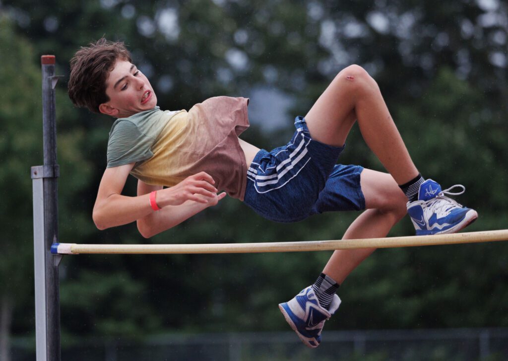 Zeb Payne, 13, leaps over the high bar, his blue sneakers slightly touching the high bar.