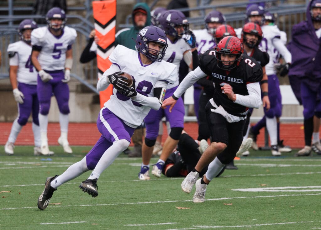 Nooksack Valley's Bennett DeLange runs for a 47-yard touchdown as a defender runs alongside in an attempt to stop him.