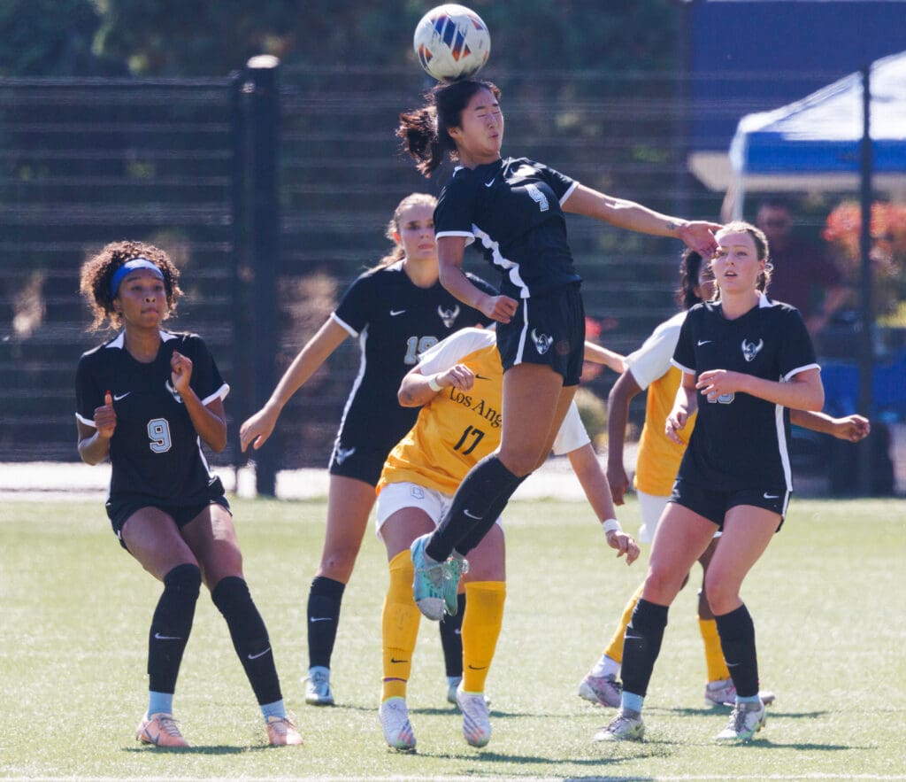 Western Washington University’s Morgan Manalili leaps into the air to head the ball midair as other players back up to see if she hits it.