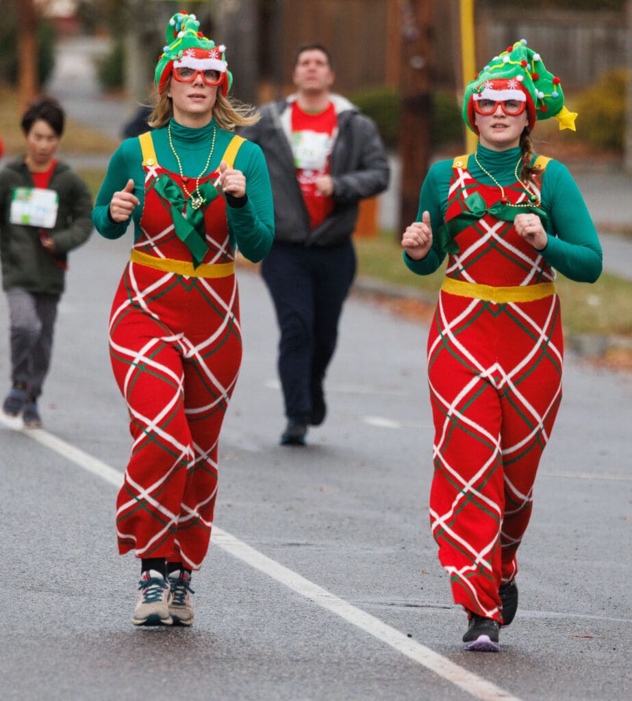 Wearing matching christmas themed outfits, Melanie Dickinson and Jillian Neff run alongside each other.