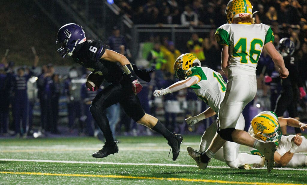 Anacortes running back Brady Beaner rushes past three defenders, leaving them to fall on the grassy field.