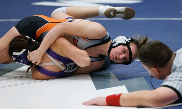 Blaine's Lucyanna Dahl tries to pin her Anacortes opponent to the blue mat as a referee lowers himself on the ground to their levels.
