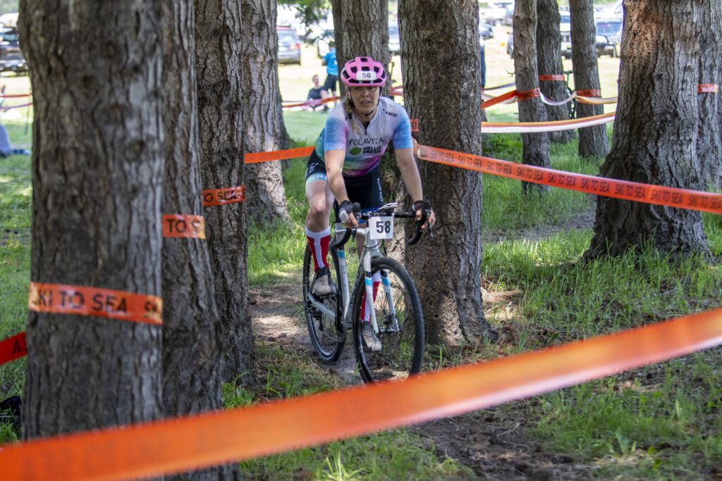 Cyclocrosser Olga Magun weaves through trees, the path closed off with bright orange tape labeled Ski to Sea.