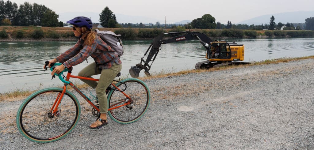A biker rides by as an excavator drops riprap armor along the levee of the Skagit River on Friday