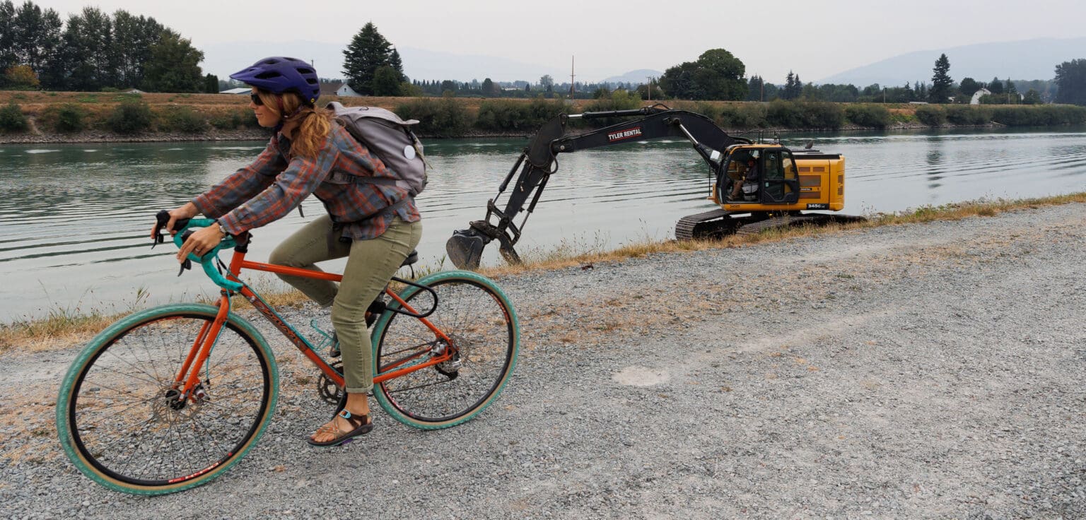 A biker rides by as an excavator drops riprap armor along the levee of the Skagit River on Friday