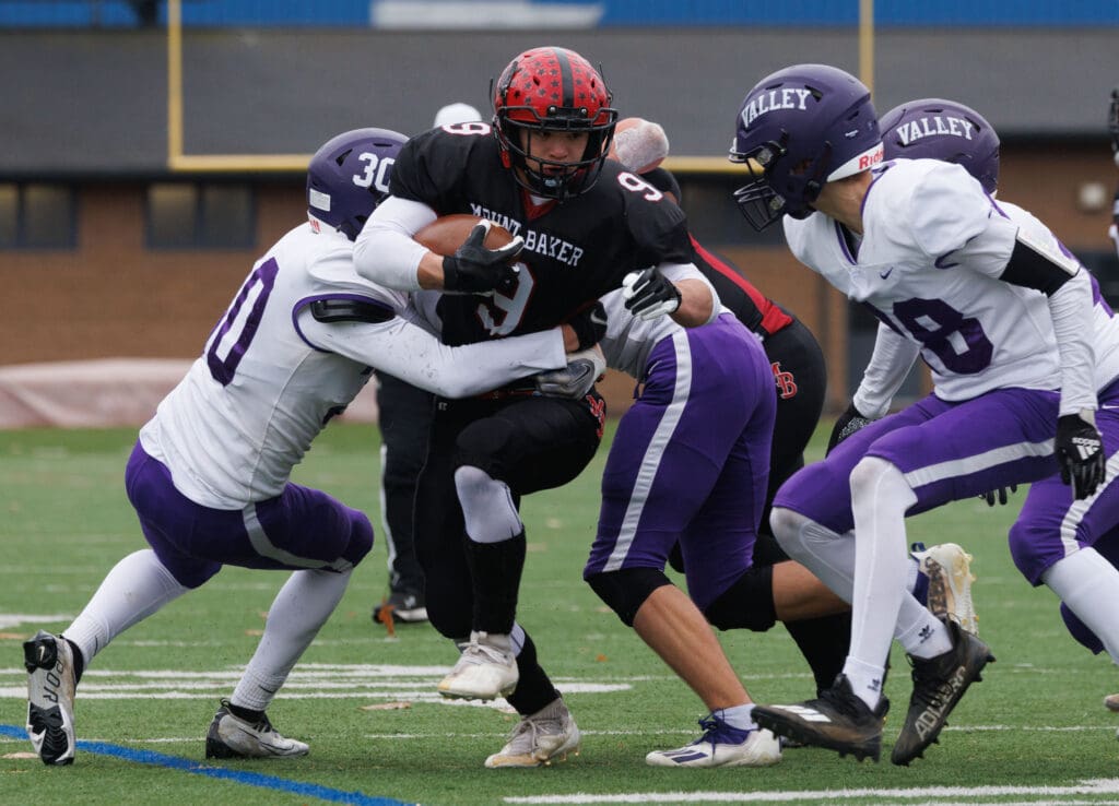 Nooksack Valley defenders surround Mount Baker's Marcques George as some tackle him from the torso.