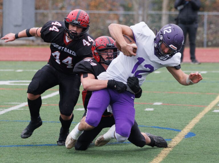 Mount Baker's Alex Maloley grabs hold of Nooksack Valley quarterback Joseph Brown by the waist as his teammate rushes to help behind him.