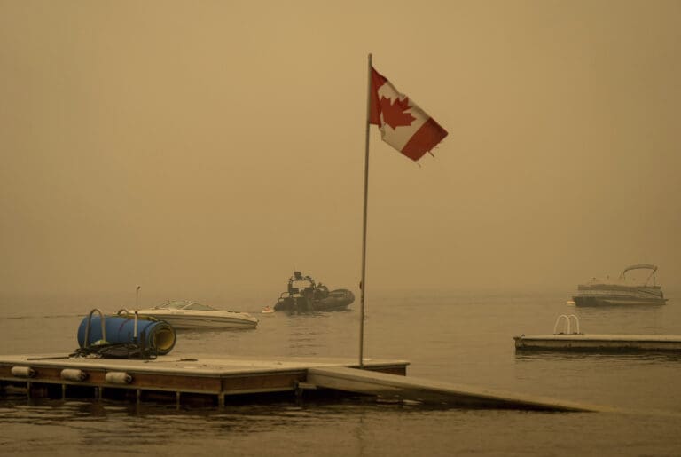 Thick smoke from the Lower East Adams Lake wildfire fills the air around a Canadian flag fluttering in the wind as Royal Canadian Mounted Police officers on a boat patrol Shuswap Lake