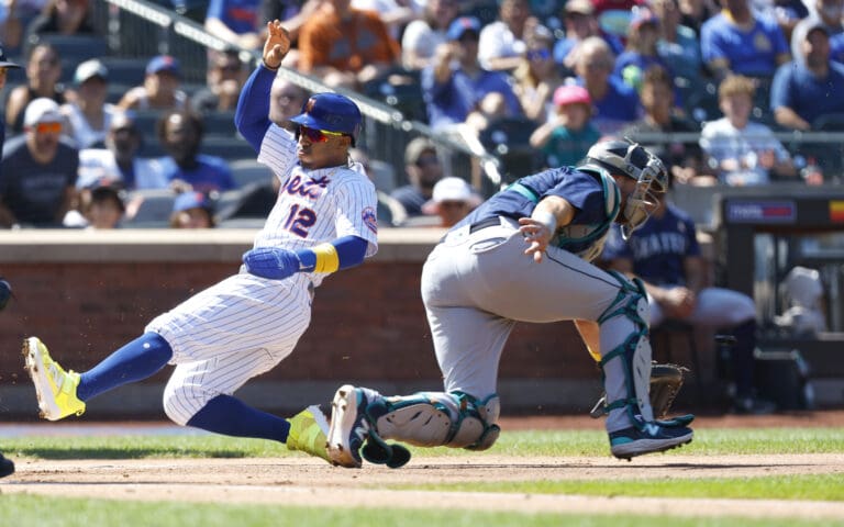 New York Mets' Francisco Lindor (12) beats the throw to Seattle Mariners catcher, Cal Raleigh, who is leaning forward.