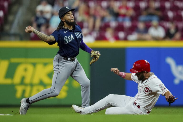 Seattle Mariners' J.P. Crawford, left, forces out Cincinnati Reds' Nick Martini as he pulls back his arm to throw the ball as the other player slides on the grass.
