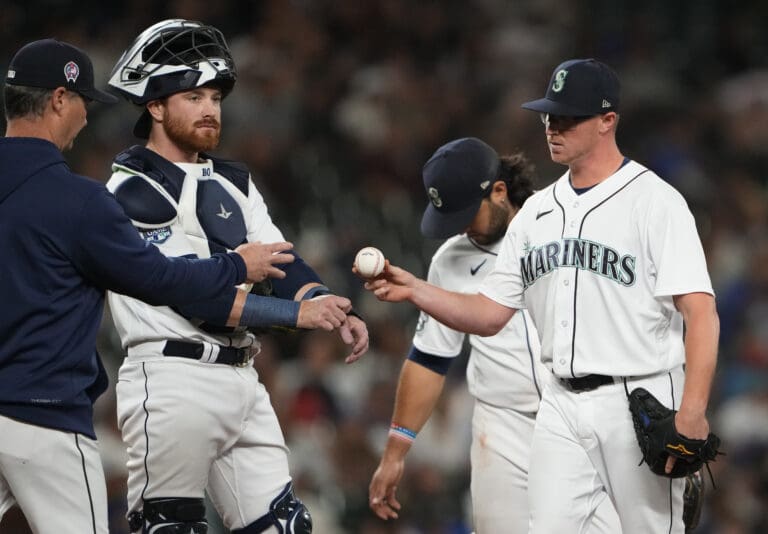 Seattle Mariners relief pitcher Trent Thornton, right, gives the ball to manager Scott Servais, left as another player also reaches for the ball.