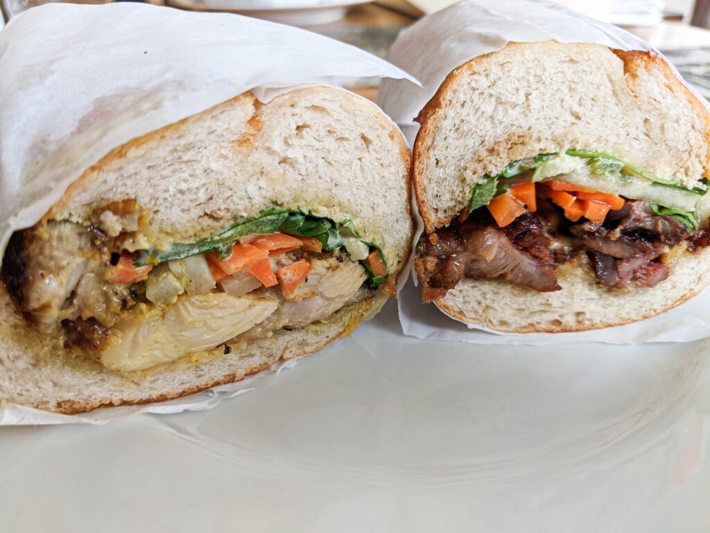 A cross-section cut of a delicious looking bánh mì sandwich filled with meat, veggies, and sauce.