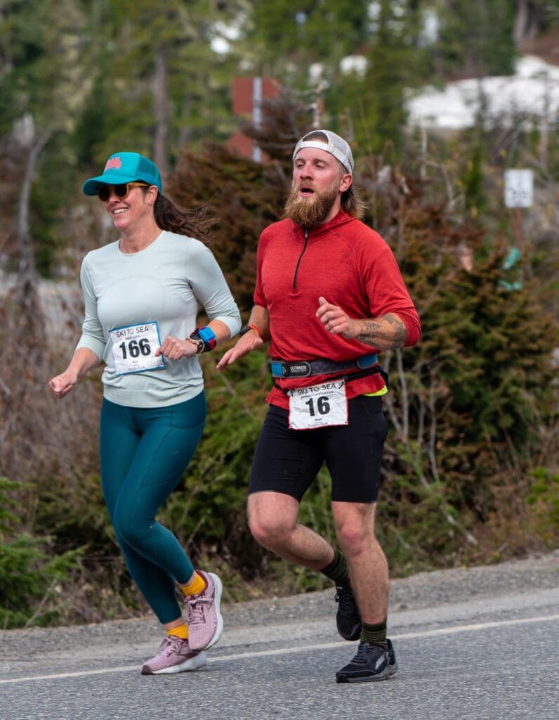 Cory Brunhaver runs down Mount Baker Highway after completing both ski legs back-to-back next to another runner.