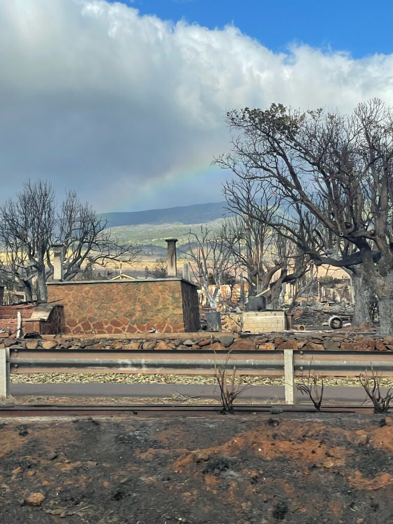 A rainbow shines behind fire damage in Lahaina.