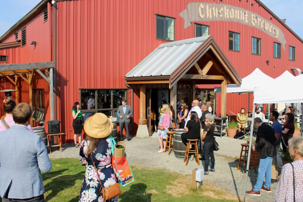 A collection of people gather outside of a red building that says "Chuckanut Brewery."