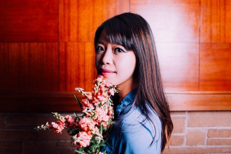 Lauded poet and Western Washington University creative writing instructor Jane Wong posing with bright pink flowers.