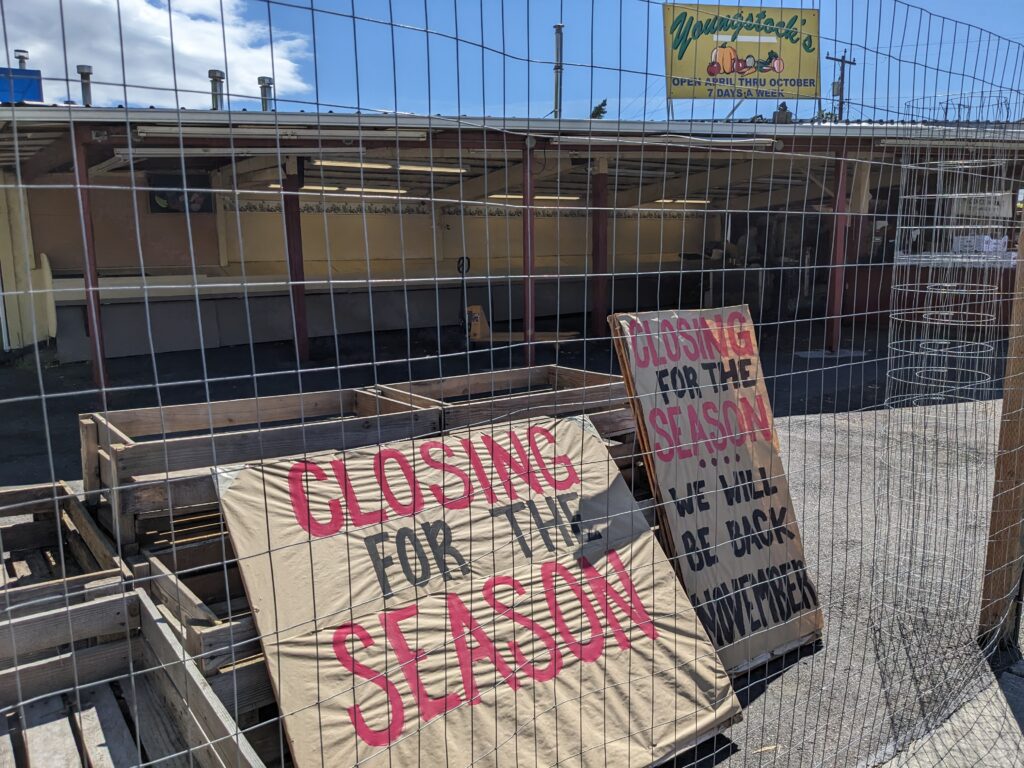 Signs read "closing for the season" behind a grate at a prodcue stand.