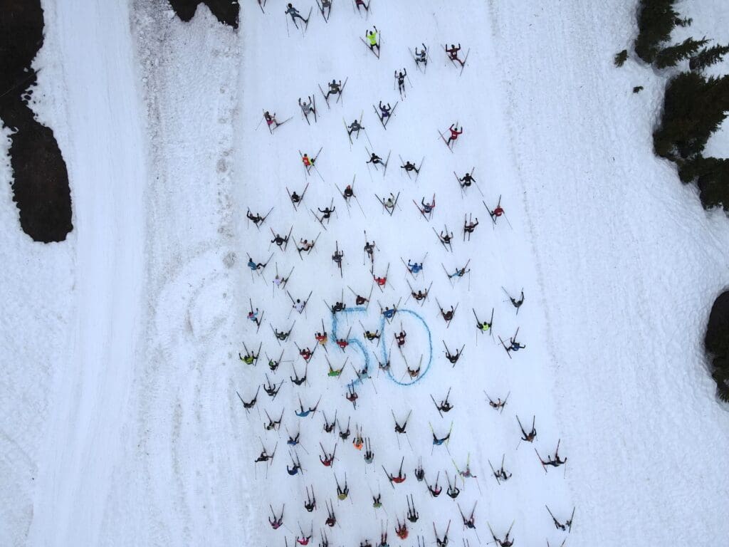 A blue 50 spray-painted in the snow to mark the 50th anniversary as many skiers ski past it.