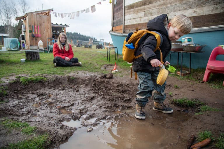 Teacher Lizzy Chandler, left, watches Mac play in the mud pit Feb. 13 at Barefeet Farm School. The outdoor school operates year round, rain or shine.